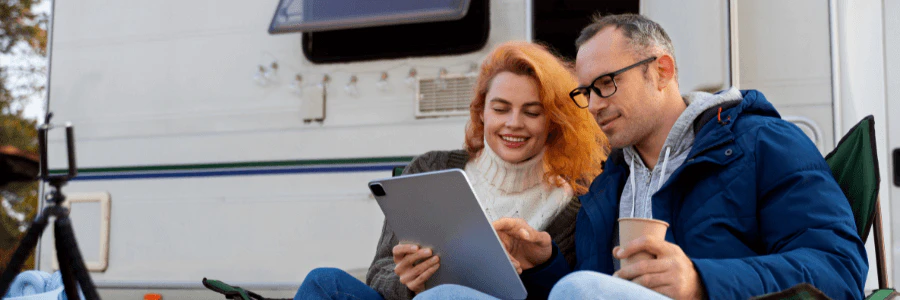A couple hanging out by a white modern RV home parked outdoors