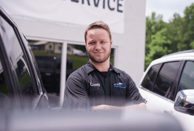 Corey standing between 2 used car for sale in a dealership parking lot