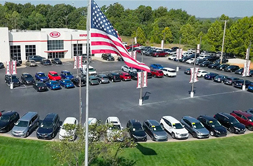 an american flag infront of a car dealership selling new and used cars