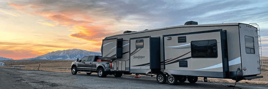 A truck on the road hauling an RV with mountain view background