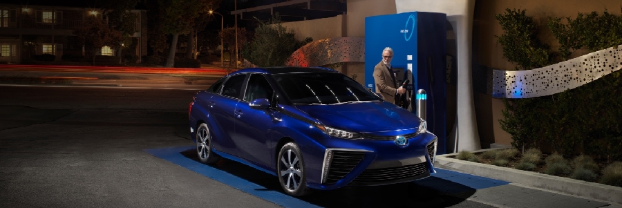 A man fills up a blue Toyota at a Hydrogen pump at night