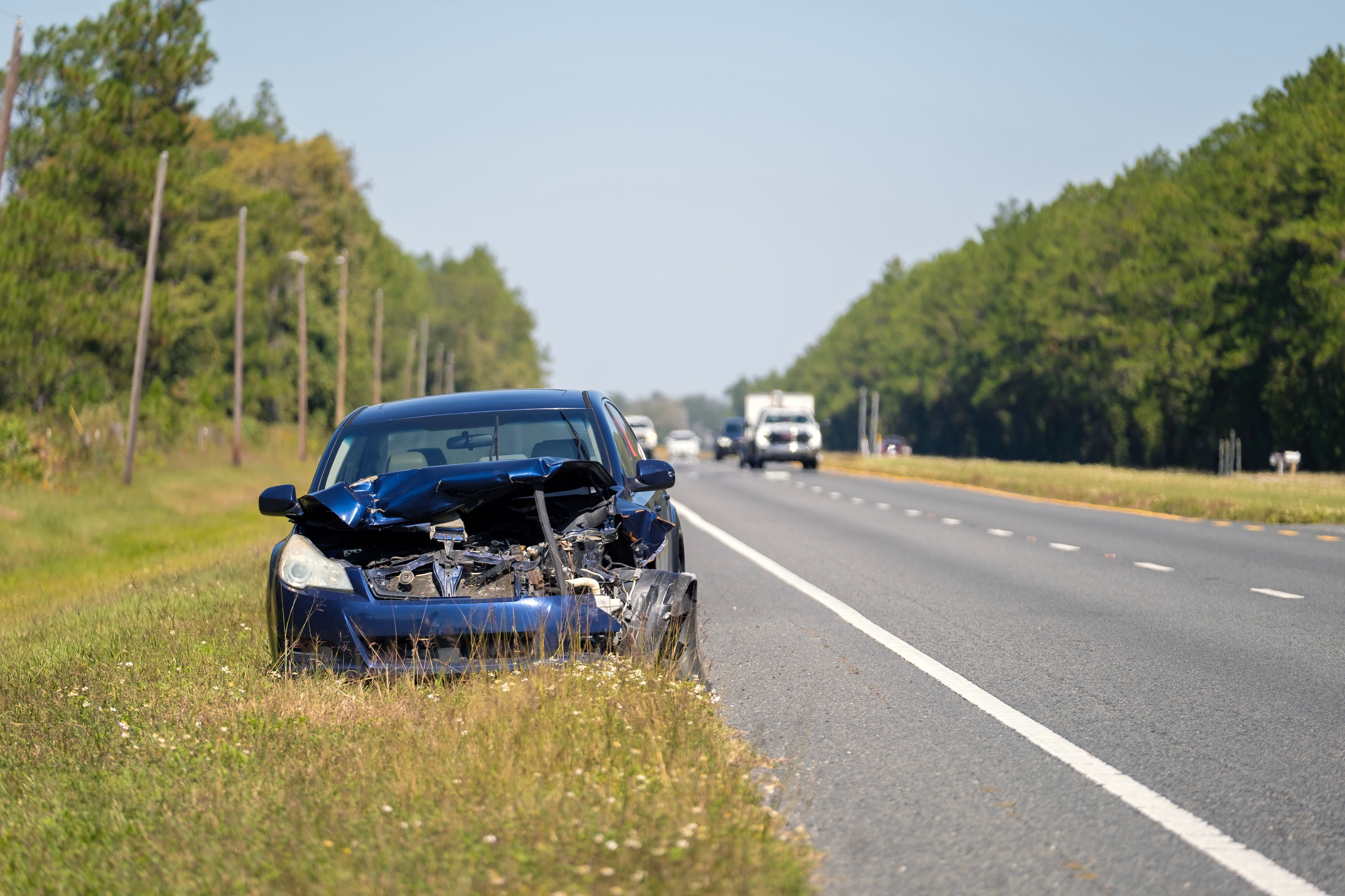 Damaged blue car with a crumpled front end parked on the roadside near a hi