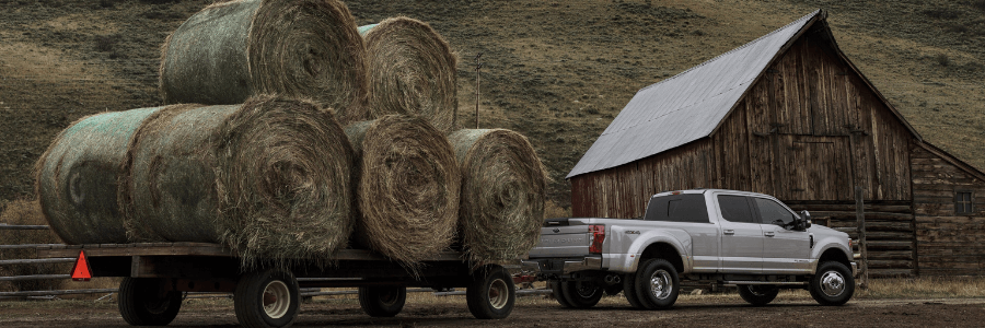 Ford f-350 truck towing 5 large bales of hay in the country-side.