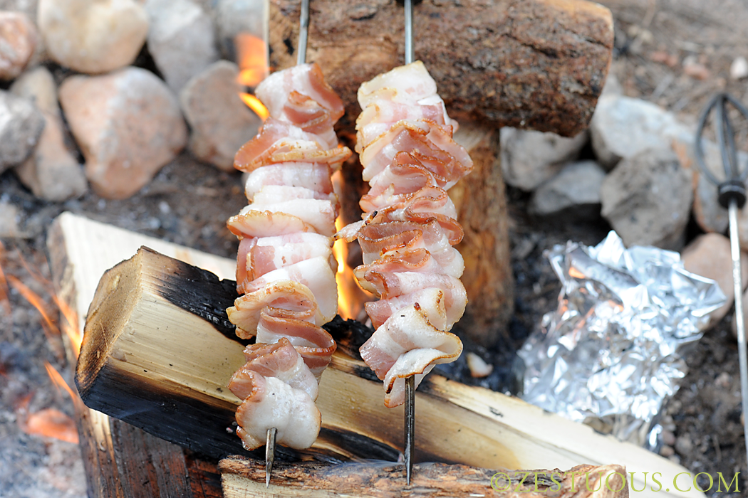 bacon over a campfire rolled up on skewers