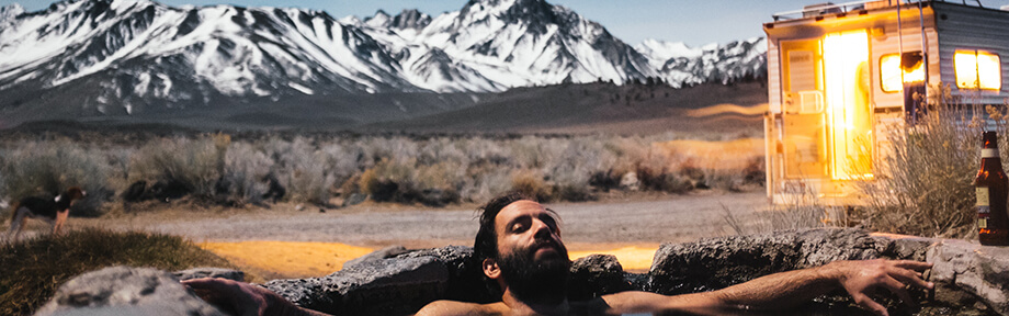 Man lounging in a hot spring by his stylish RV