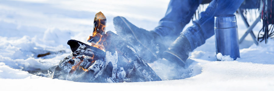 man relaxing by winter campfire with coffee