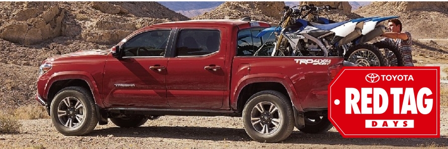 A red Toyota Tacoma sits in mountains with dirt bikes in bed