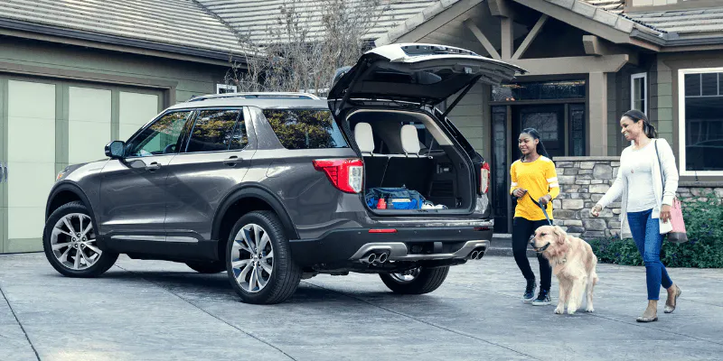 other and daughter with a golden retriever loading gear into a gray Ford Explorer in a driveway