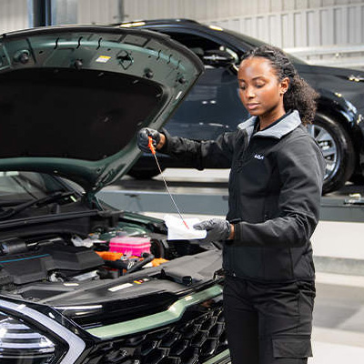 female technician checking oil on Kia vehicle