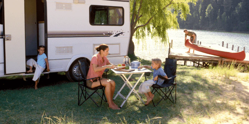 Family camping beside an RV at a lakeside after RV repair