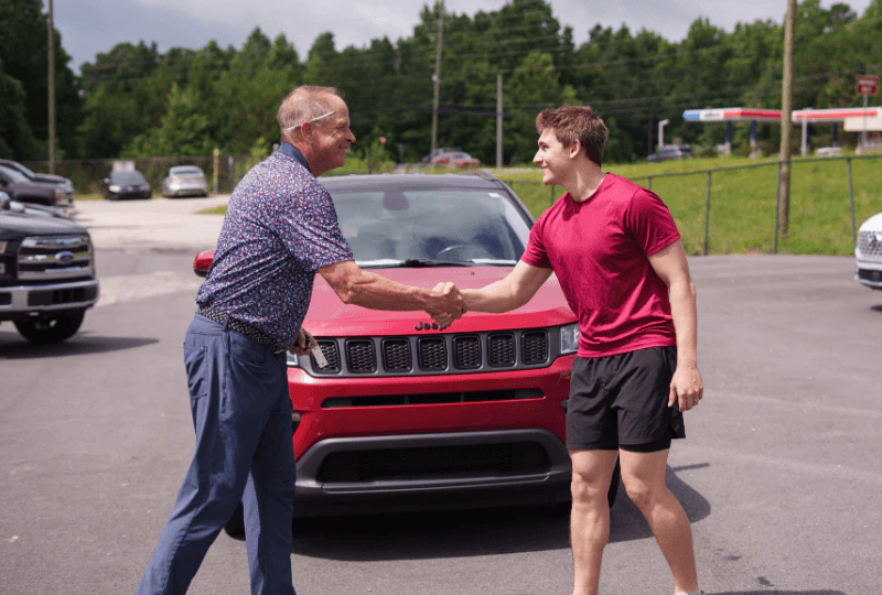 A guy and a salesman shaking hand in front of a red car