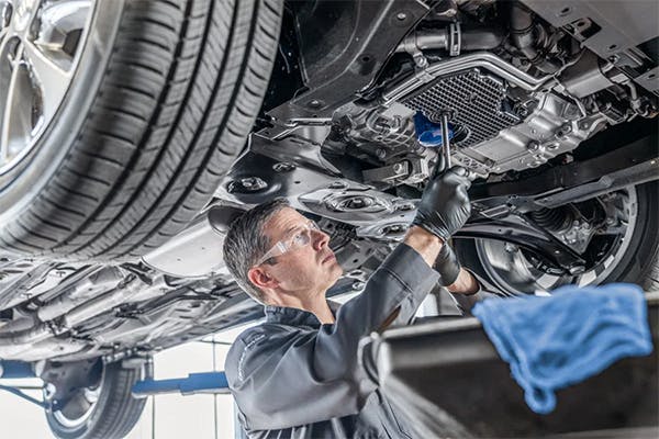 male service technician performing an oil change under a vehicle