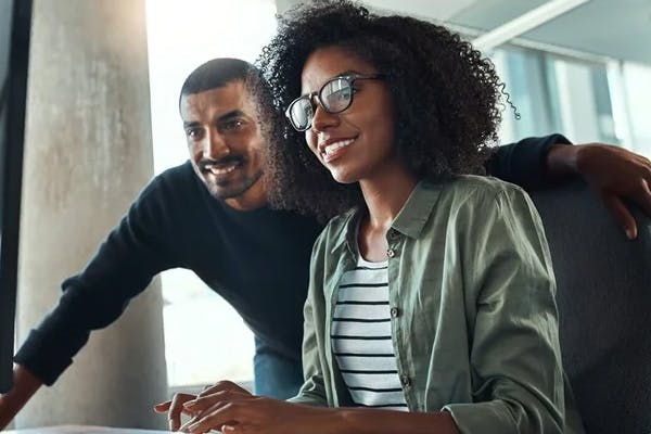 woman on a computer with their partner watching over their shoulder