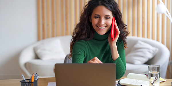 woman on the phone smiling while on their laptop in living room