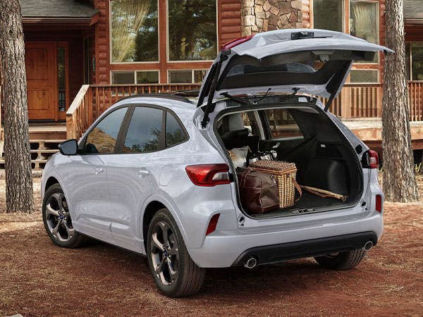 a ford car with an open trunk is parked in front of a cottage