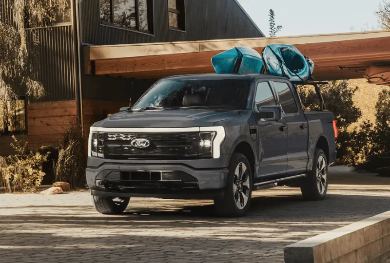 Gray Ford F-150 Lightning electric truck with kayaks on a rack outside a modern home