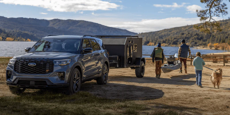 Blue Ford Explorer towing a camper trailer near a lake with a family and dog