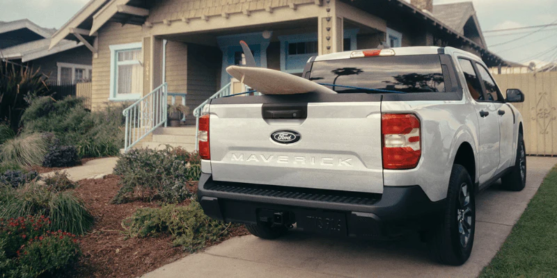 Rear view of a Used white Ford Maverick with a surfboard in the bed parked in a driveway