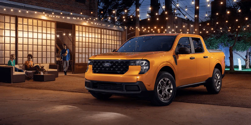Yellow Ford Maverick truck parked outside a lit building at night with string lights