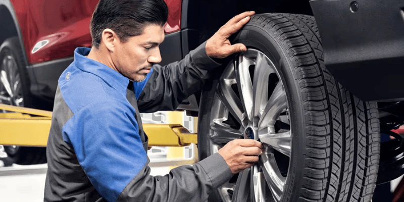 Ford technician inspecting a tire and wheel on a lifted vehicle in a service bay