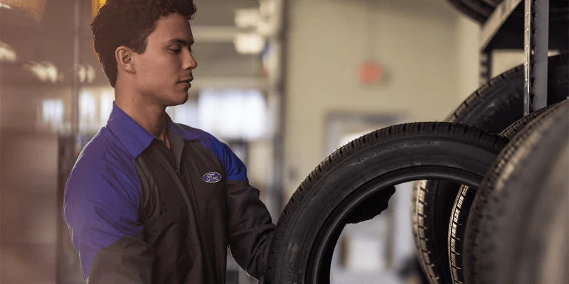 Ford service technician selecting a tire from a rack for tire rotation
