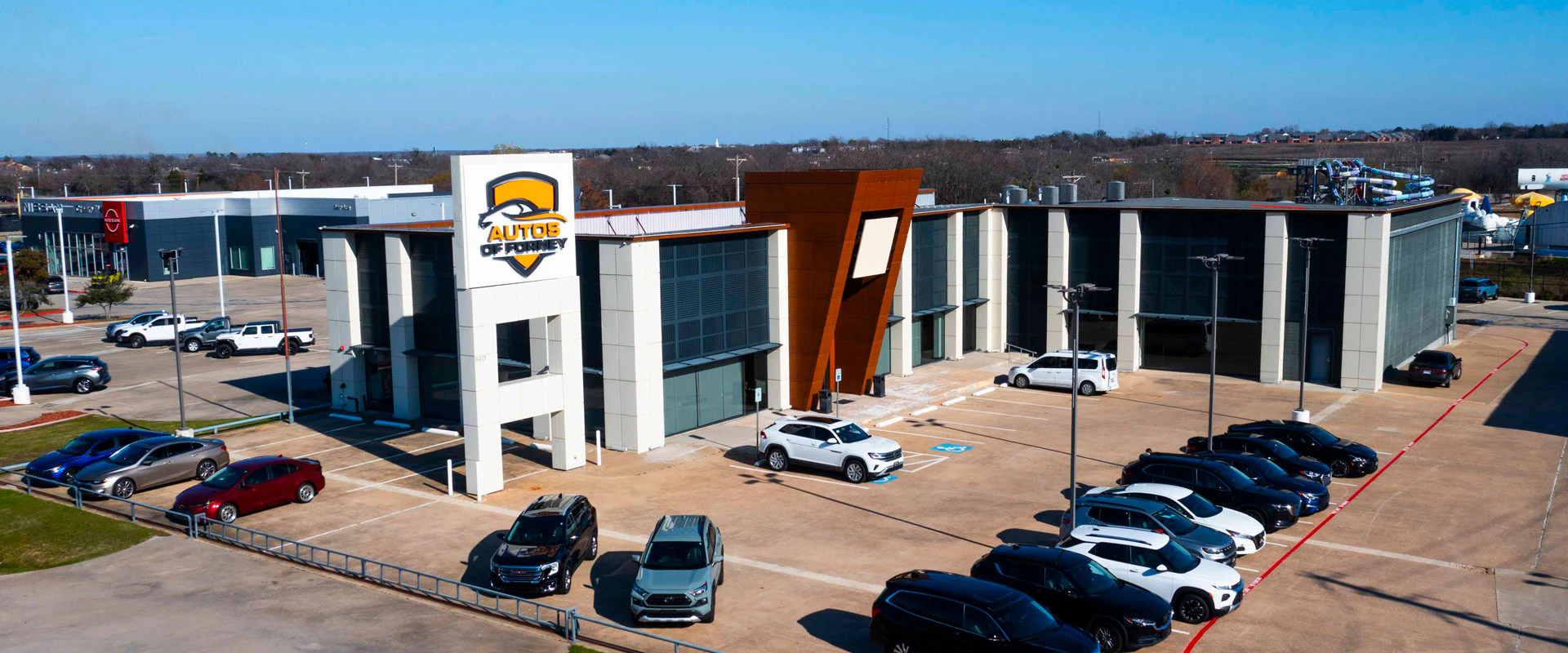 A zoomed out image of autos of ofrney dealershp building and cars for sale in the parking lot