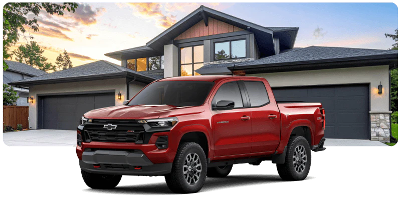Red Chevrolet Colorado truck for sale parked in front of a modern house at dusk