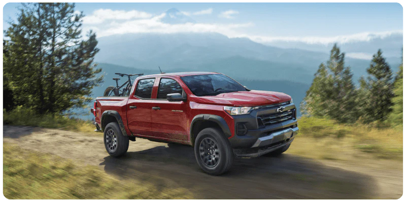Used Red Chevrolet Colorado truck for sale driving a dirt mountain road with a bike in the bed